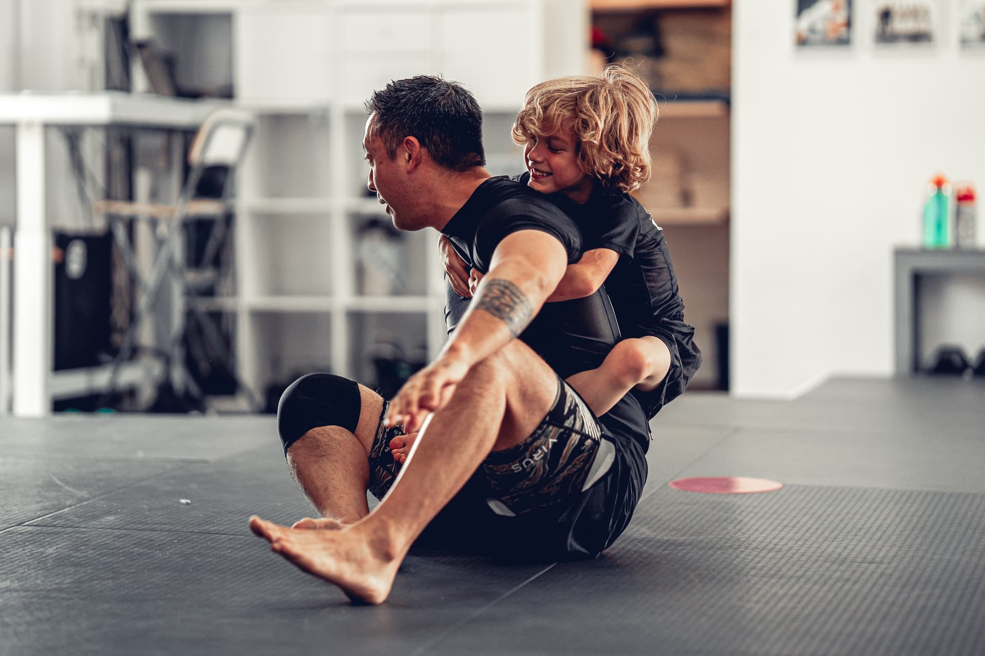 A smiling young student enjoying a playful movement drill with his coach at Del Mar Jiu-Jitsu Club.