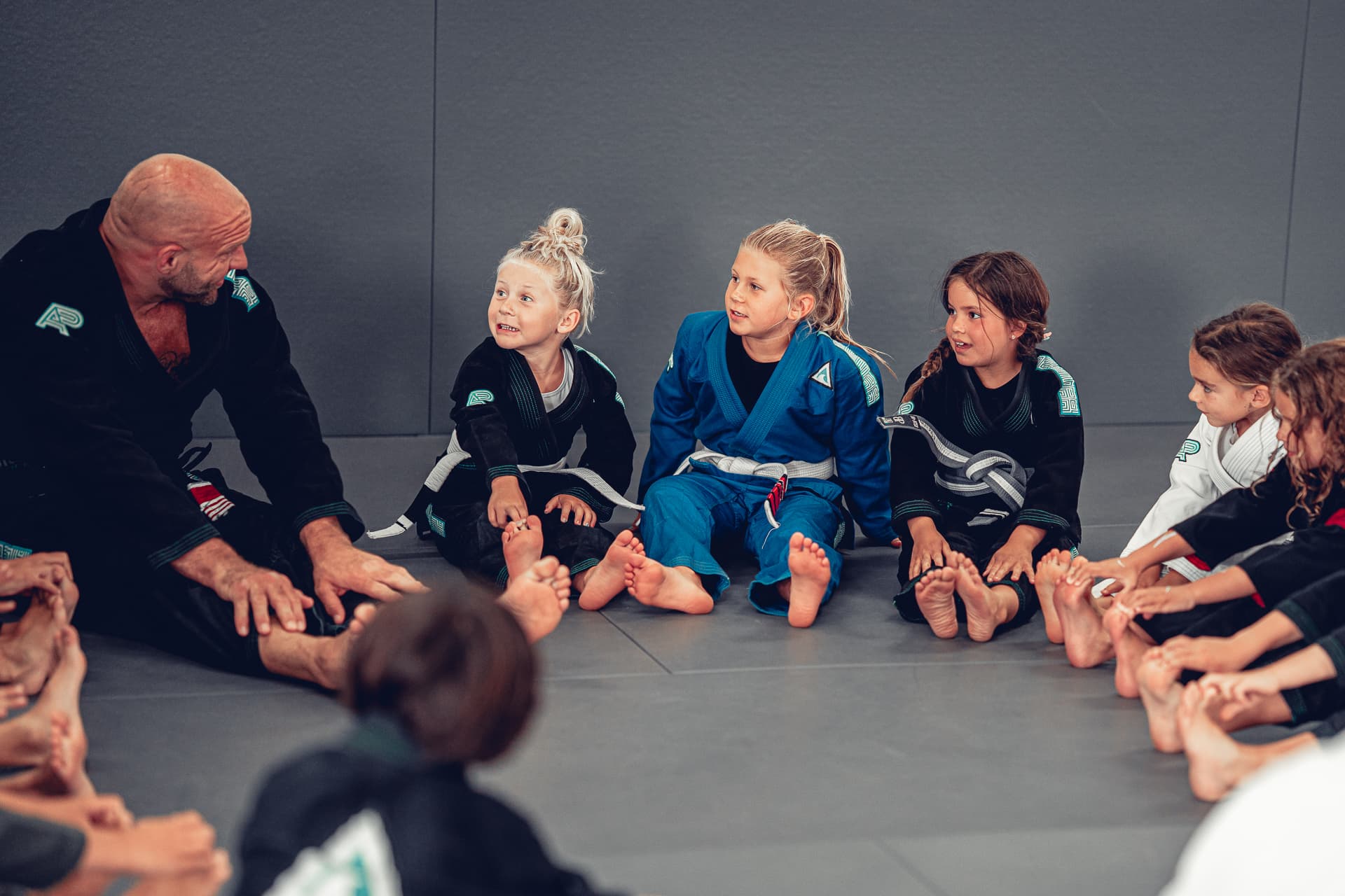 Young Jiu-Jitsu students sitting together and listening attentively to their coach.